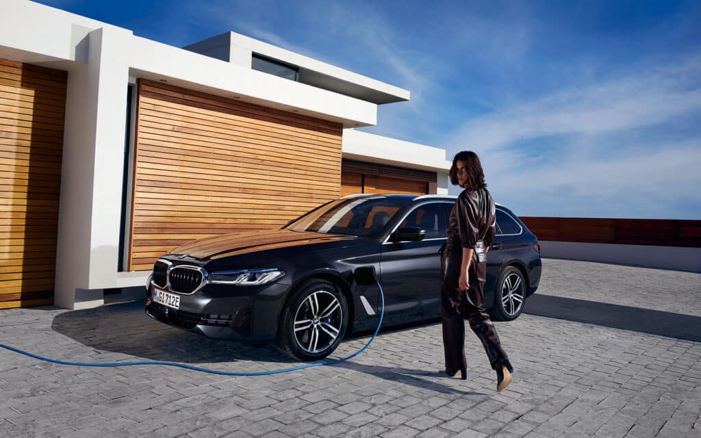 Schwarzer BMW 5er Touring PHEV an Ladestation, stilvolles Ambiente, Frau in Leder-Overall