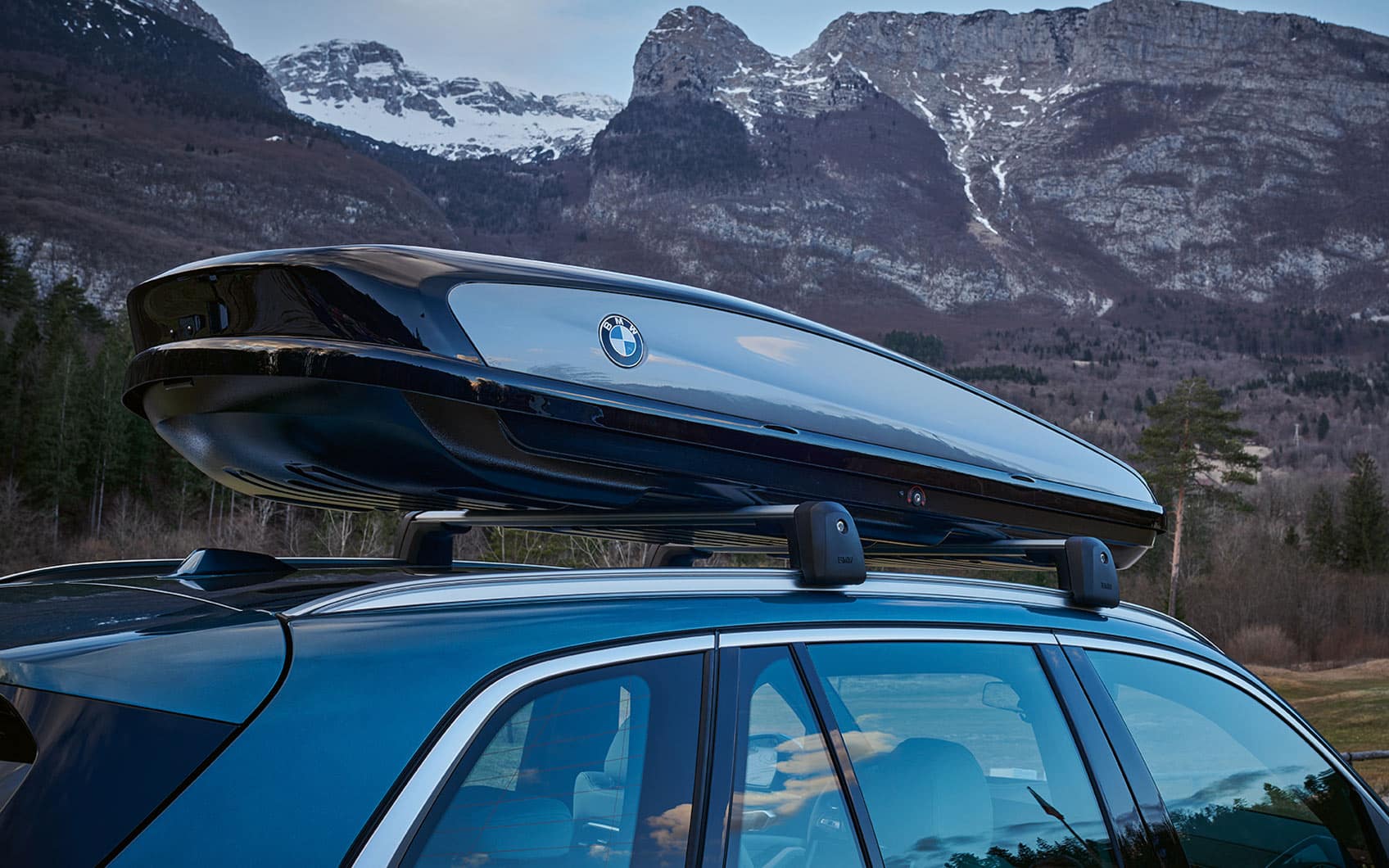 BMW mit Dachbox vor bergiger Waldlandschaft.