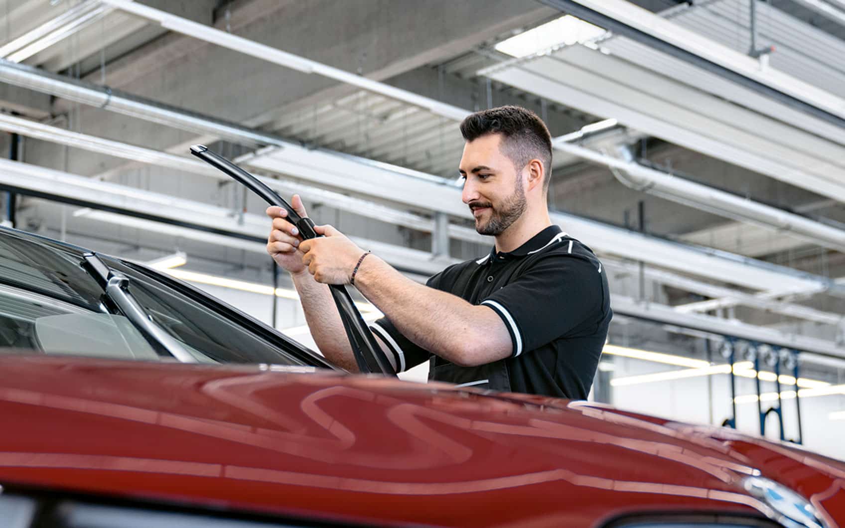 Mann wechselt Wischerblatt an rotem Auto in BMW Werkstatt.