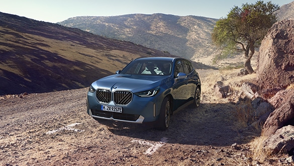 Frontaufnahme eines haltenden BMW X3 PHEV in der Farbe Blau in einer bergigen Landschaft