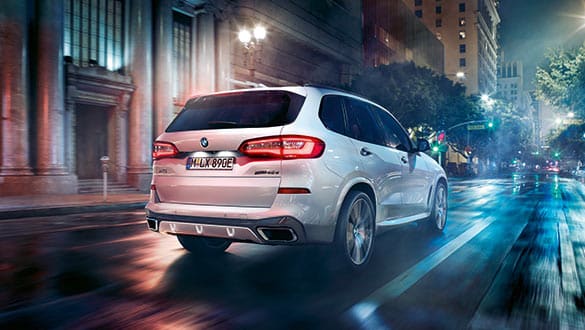 Weißer BMW X5 PHEV mit aktivierten Rücklichtern fährt auf nasser Straße, dynamische Heckansicht bei Nacht