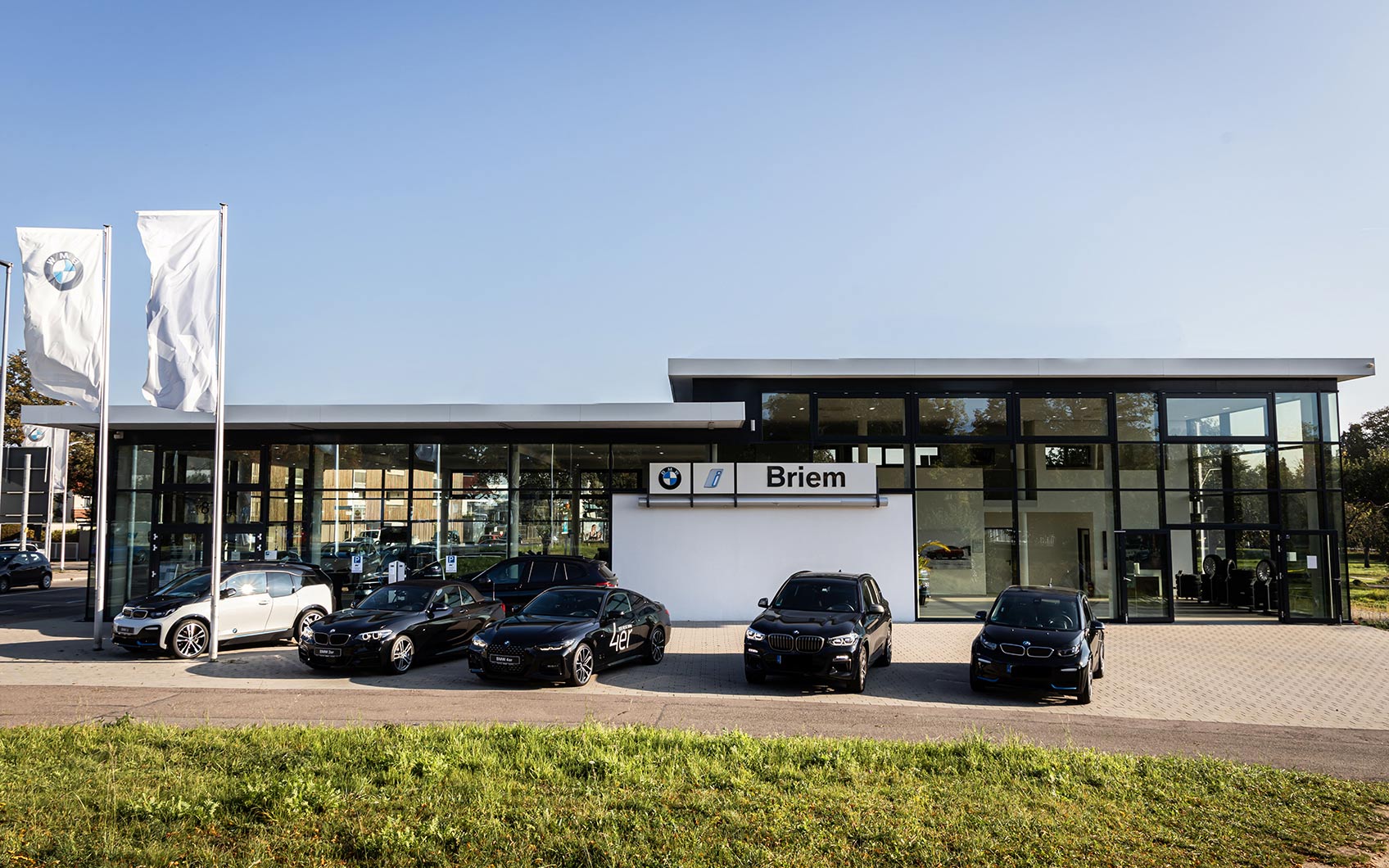Moderner BMW-Showroom mit Glasfassade und mehreren ausgestellten Fahrzeugen vor dem Gebäude.