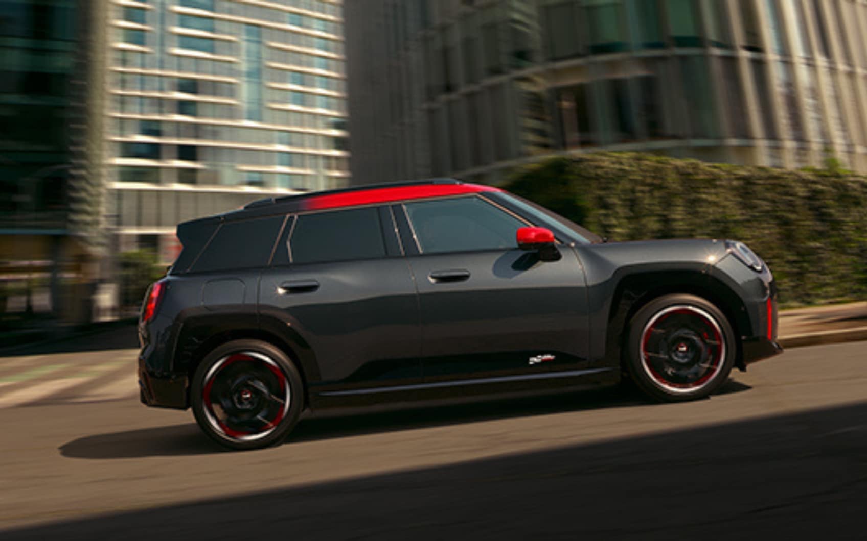 Seitenansicht eines schwarzen MINI John Cooper Works Aceman mit rotem Dach und roten Spiegelkappen in Fahrt in urbaner Umgebung