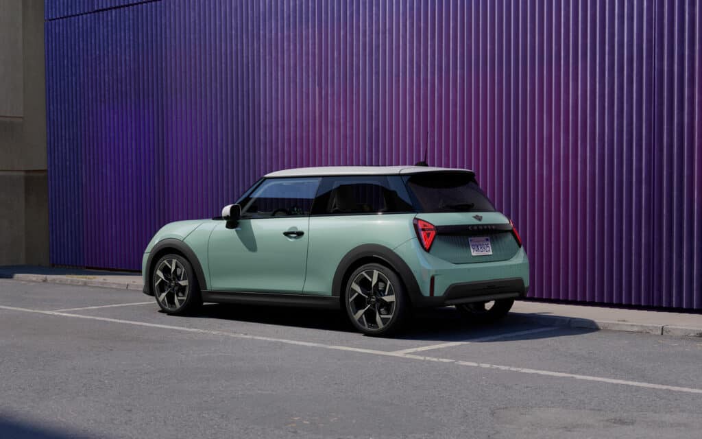 Mintgrüner Mini Cooper mit weißem Dach auf einem Parkplatz vor lila Wand