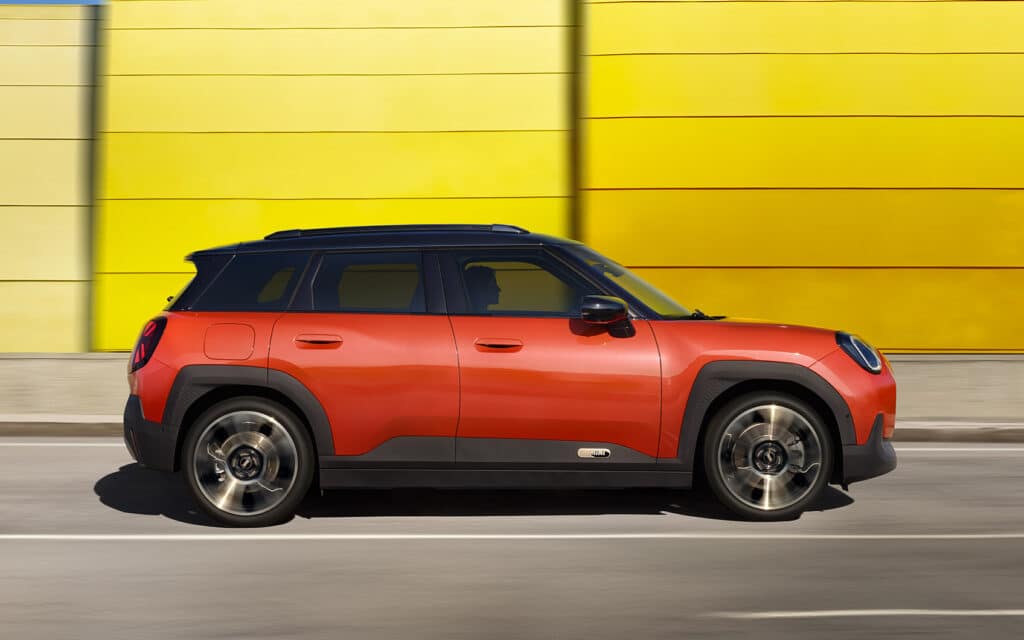 Rotes MINI SUV fährt auf Straße vor gelber Schallschutzwand entlang.