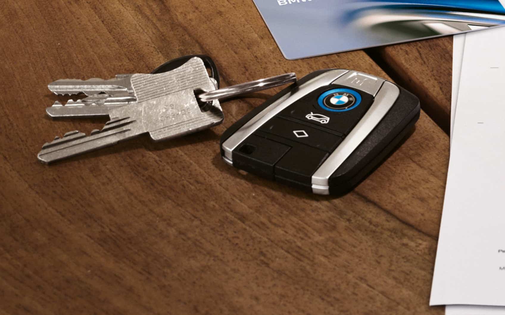 BMW-Autoschlüssel mit Hausschlüsseln, Plastikkarte und Dokumenten auf Holztisch.