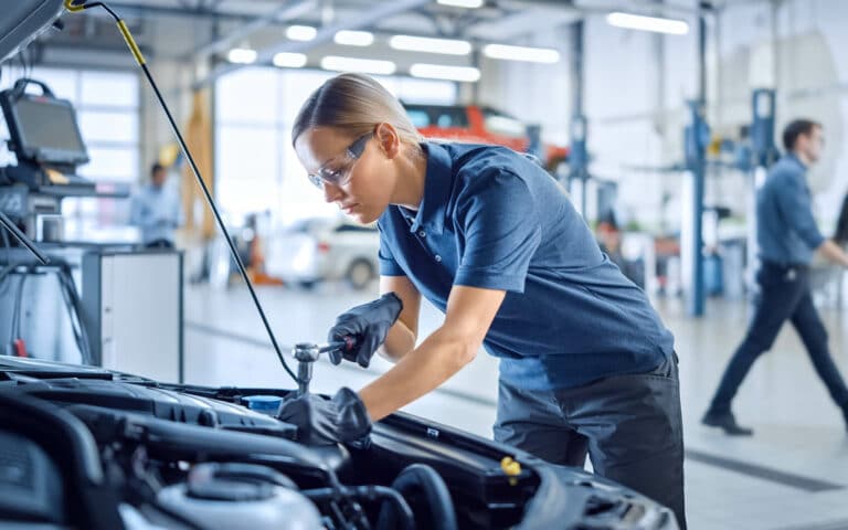 Mechanikerin arbeitet mit Ratsche am offenen Motorraum eines Autos in einer Werkstatt.