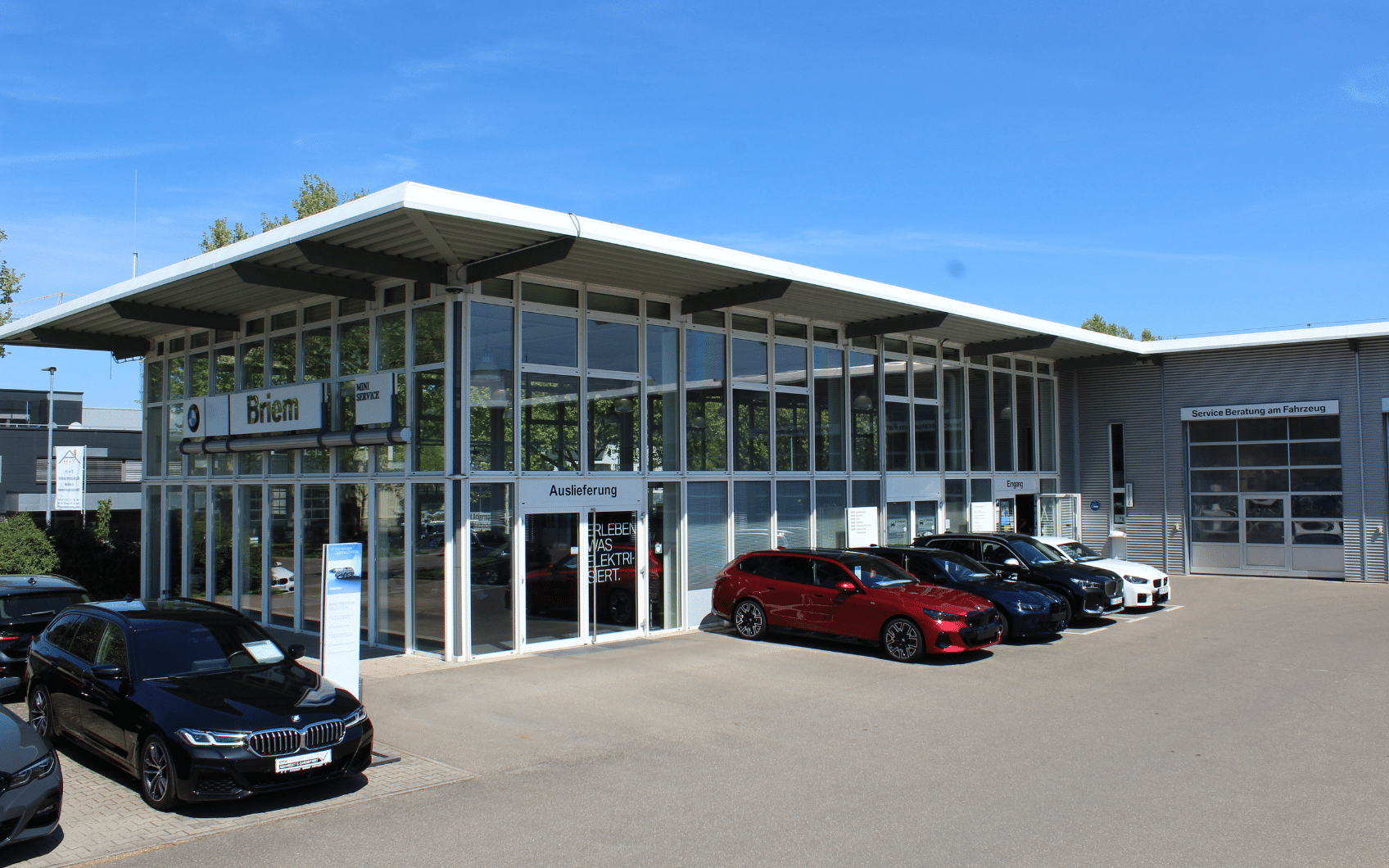 BMW Autohaus mit Glasfassade, mehreren geparkten Fahrzeugen und Beschilderung für Auslieferung und Service