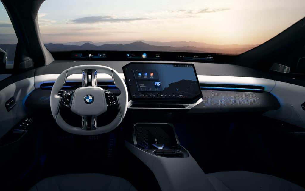 Modernes BMW-Cockpit mit futuristischem Lenkrad, großem Zentraldisplay und digitalem Armaturenbrett bei Sonnenuntergang im Hintergrund.