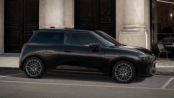 Seitenansicht eines MINI Cooper Electric Blackyard parkend vor einem historischen Gebäude mit Säulen und dunklen Türen