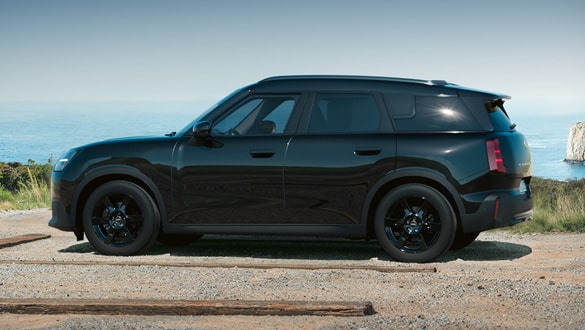 Seitenansicht eines MINI Countryman Electric Blackyard auf einem Küstenweg mit Klippen und Meer im Hintergrund.