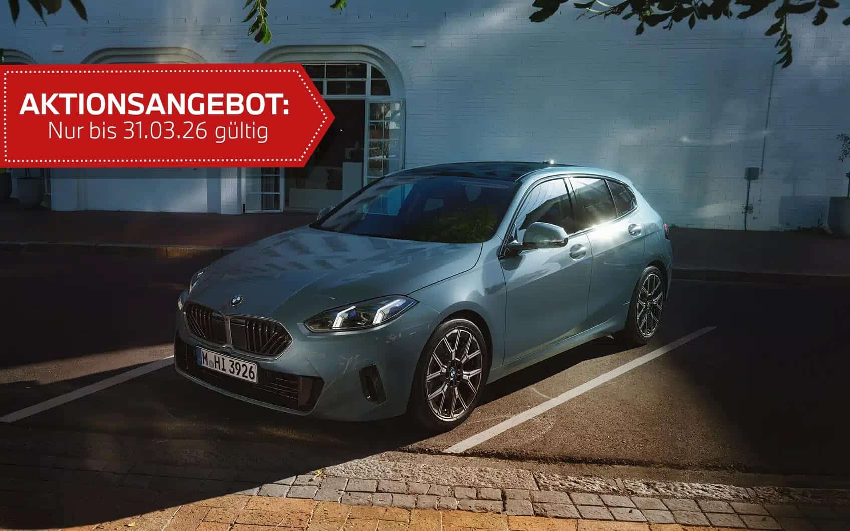 BMW steht auf Hof mit Pflastersteinen. Im Hintergrund ist ein weißes Haus zu sehen. Oben ragen grüne Äste eines Baumes ins Bild. Mit rotem Störer.