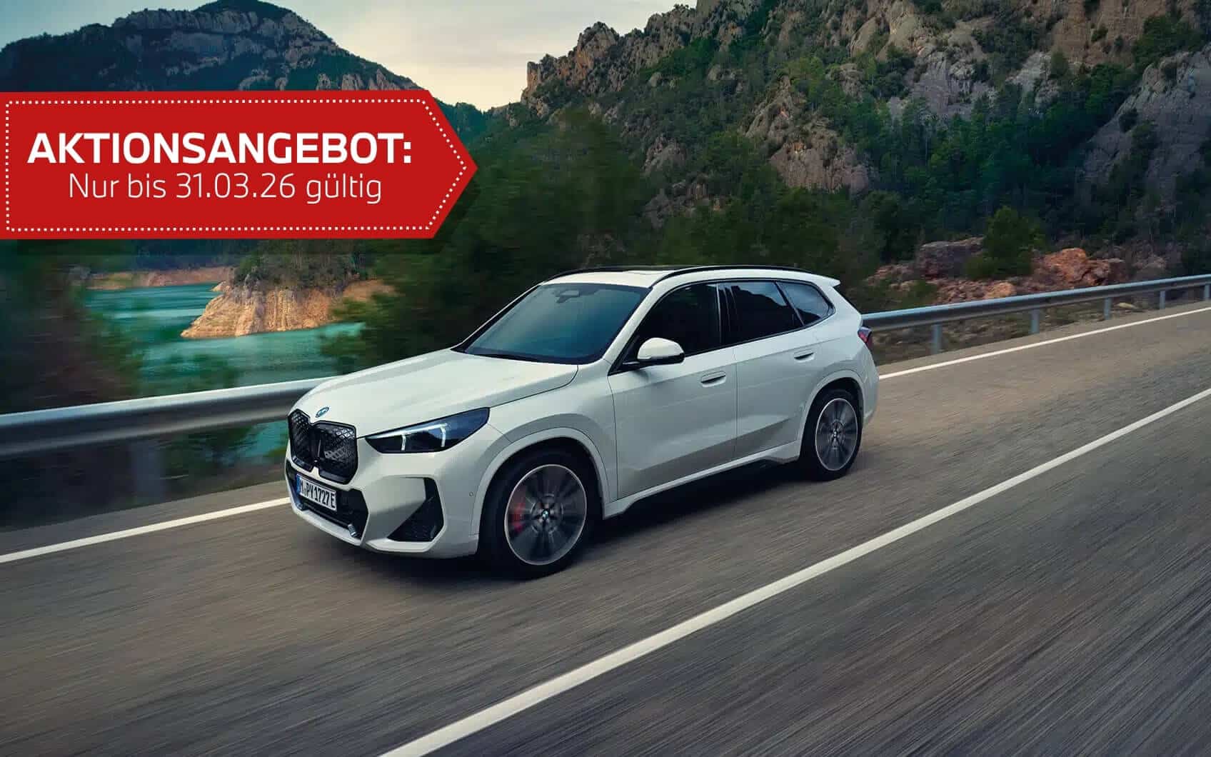 Weißer BMW iX1 auf Straße. Im Hintergrund ist eine begrünte Küstenlandschaft zu sehen. Mit rotem Störer