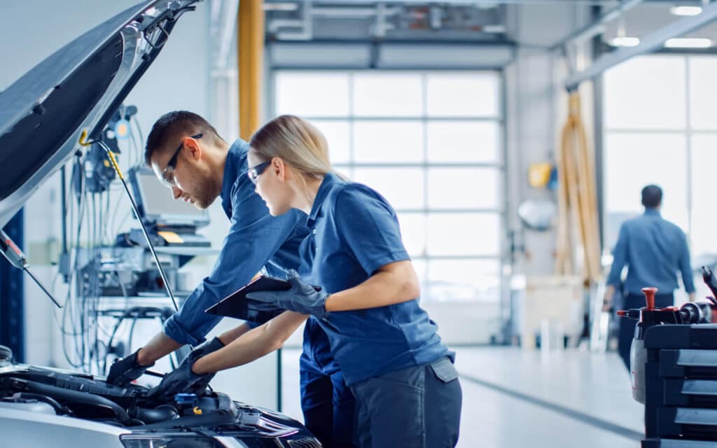 Kfz-Mechatronikerin und Kfz-Mechatroniker prüfen gemeinsam den Motorraum.