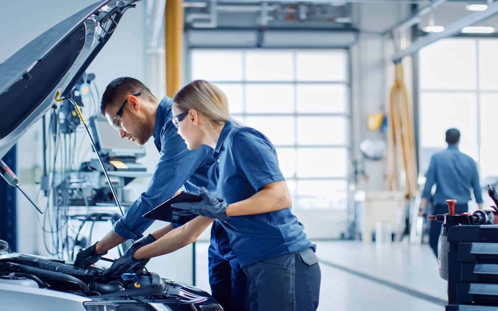 Kfz-Mechatronikerin und Kfz-Mechatroniker prüfen gemeinsam den Motorraum.